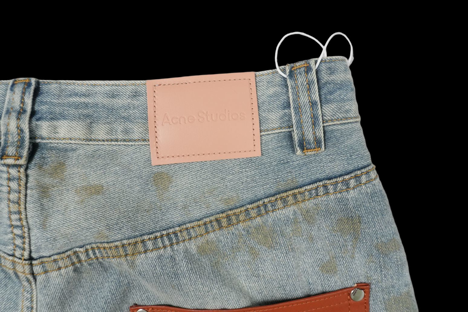 Acne Studios light wash wide-leg jeans with mud-dye distressing and a pink leather logo patch.