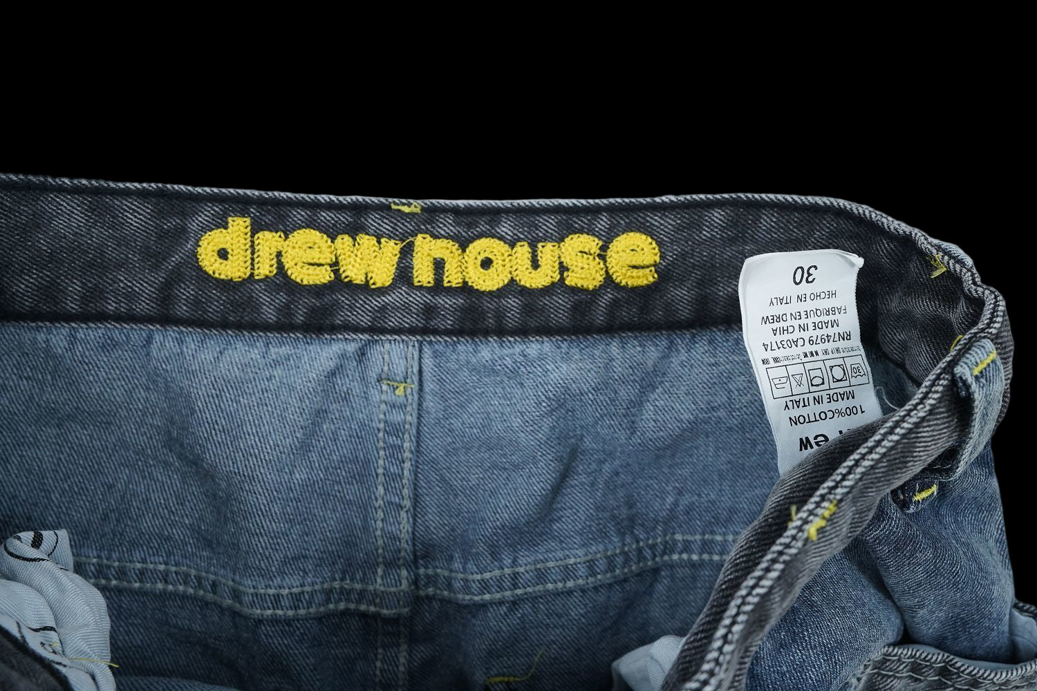 Drew House wide leg denim jeans with yellow embroidered logo and care tag.